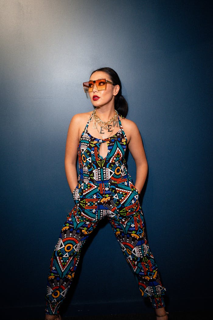 Fashionable woman in vibrant jumpsuit and sunglasses posing confidently indoors.