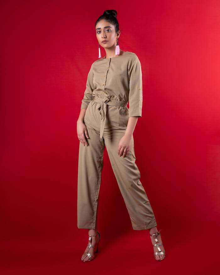 Fashion portrait of a woman in a khaki jumpsuit against a vibrant red background.