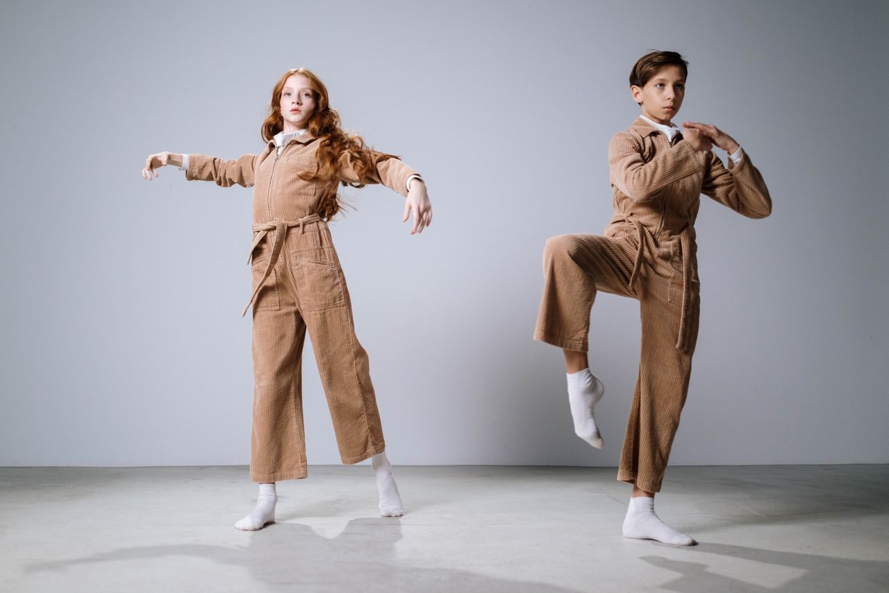 Two young dancers in coordinated outfits performing contemporary dance indoors.