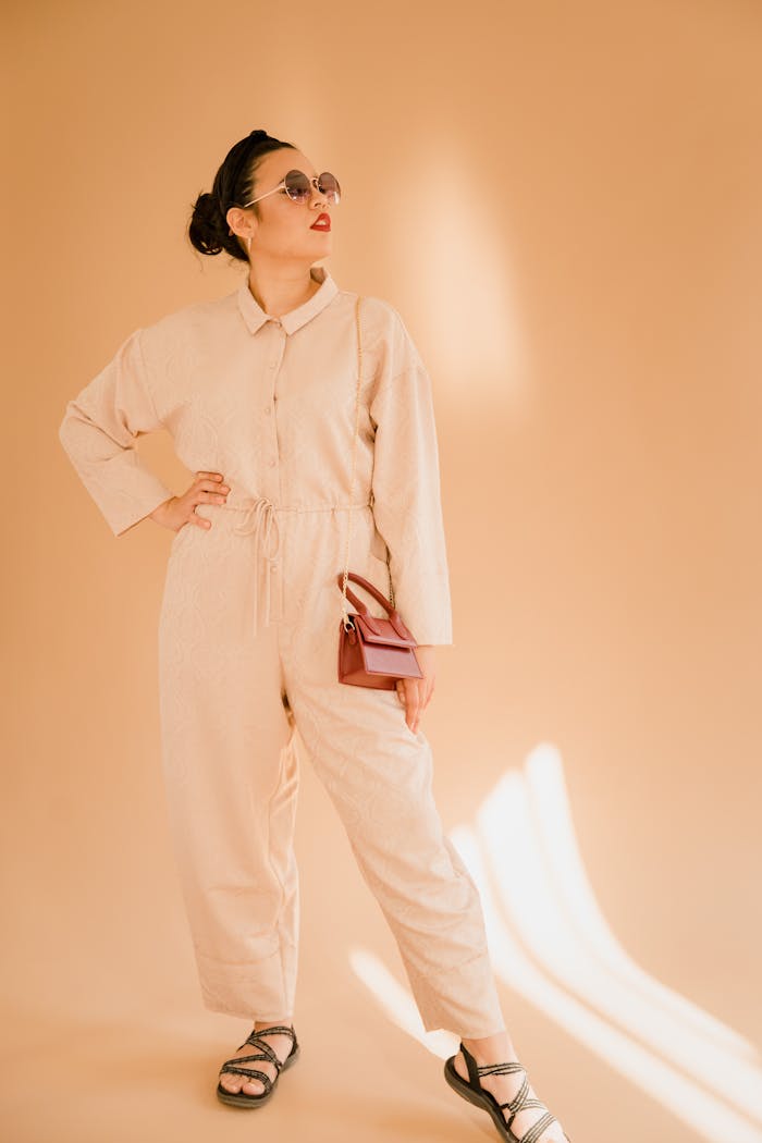 Fashionable woman in beige jumpsuit with sunglasses in a stylish pose.